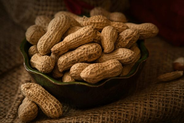 A rustic bowl filled with whole peanuts resting on a burlap cloth, evoking a natural and earthy feel.